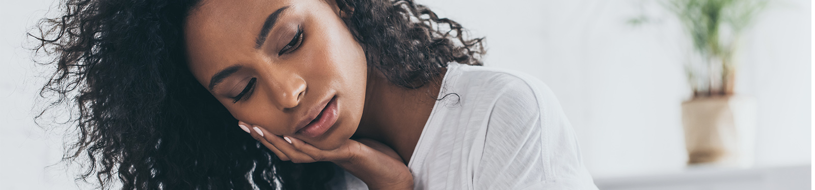 A young African American female leans on her hand with a sad and forlorn look.