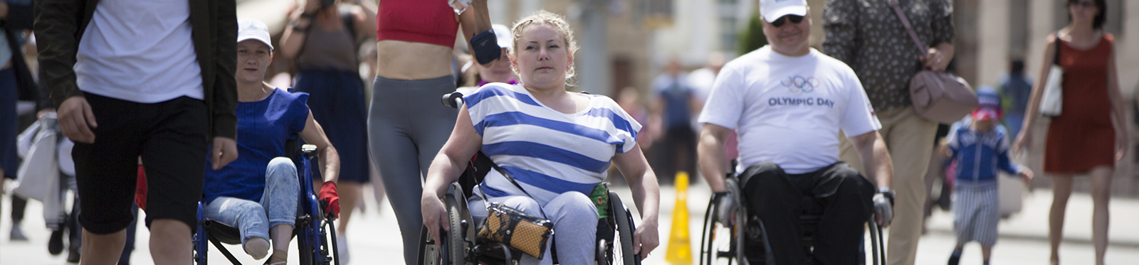 Three middle-aged people with disabilities who use wheelchairs cross a busy city street.