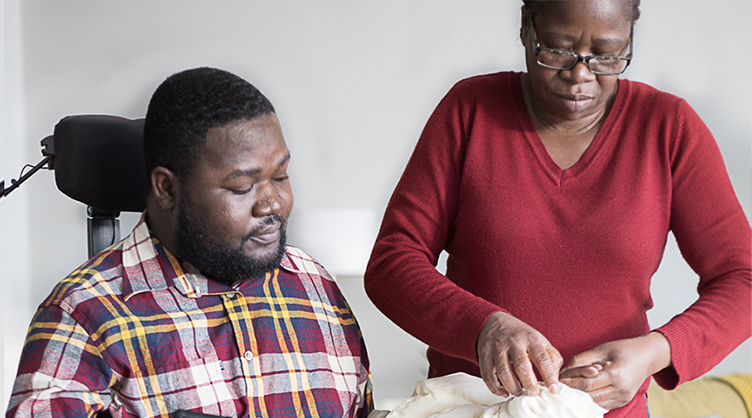 A personal support worker helping her African American client with getting dressed.