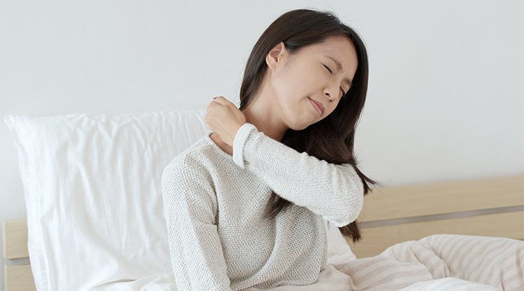 A young asian woman clutches her neck in pain while lying in bed.