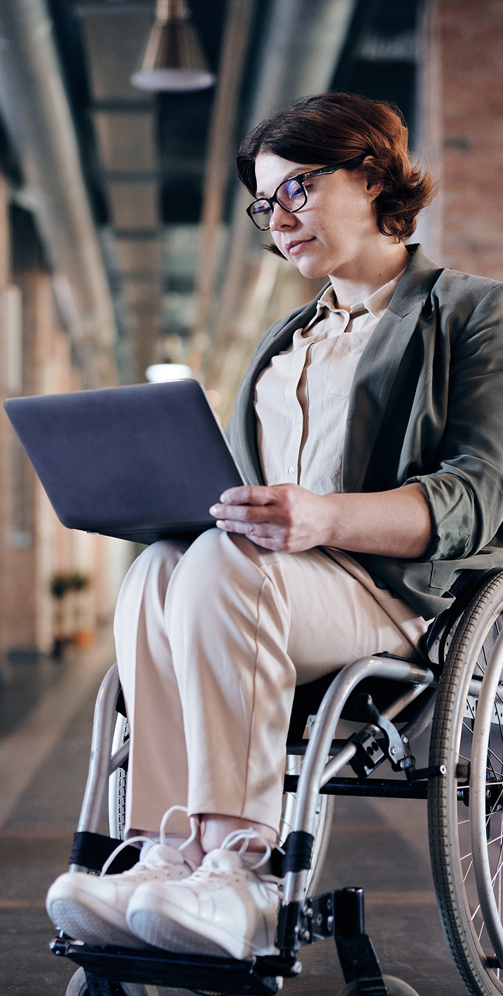 Young female who uses a wheelchair looking at her laptop in a trendy, open-concept office.