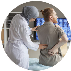 A young female doctor wearing a head scarf examines her red-headed male patient and touches his lower back.