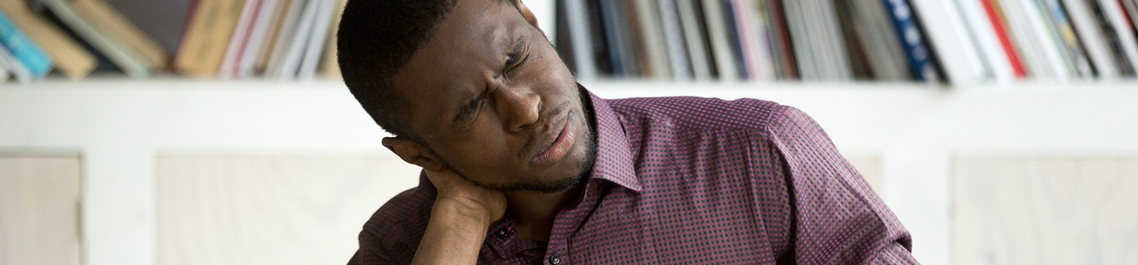 A middle-aged African American male winces in pain as he grabs his neck.