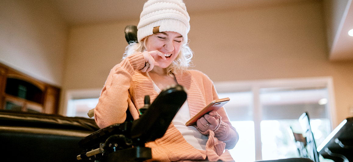 Woman who uses a power wheelchair is looking at her phone and laughing.