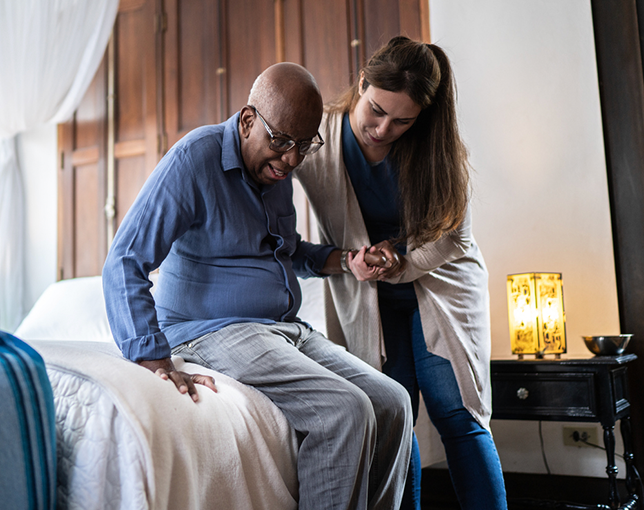 Elderly man rising from bed with help from his support worker.